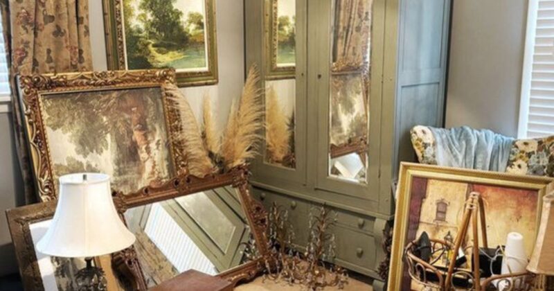 An antique painted armoire surrounded by thrifted vintage home decor such as mirrors, pastoral scenes, baskets, and sconces.