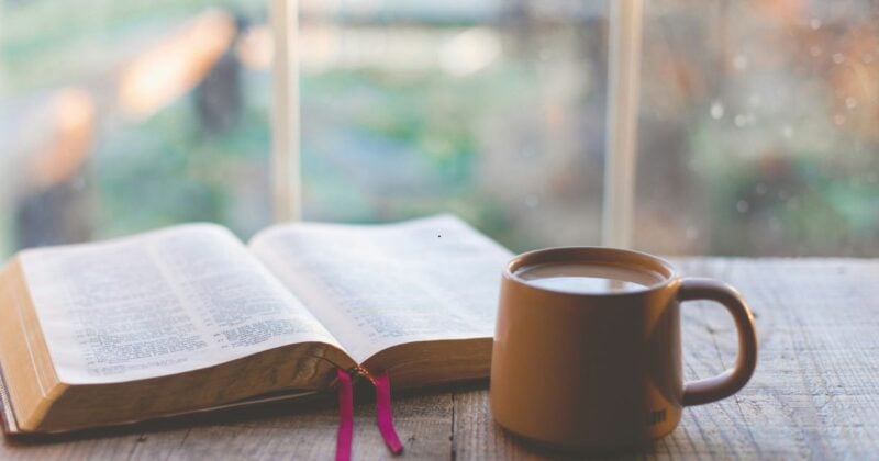 Bible open with coffee sitting near a rain splattered window